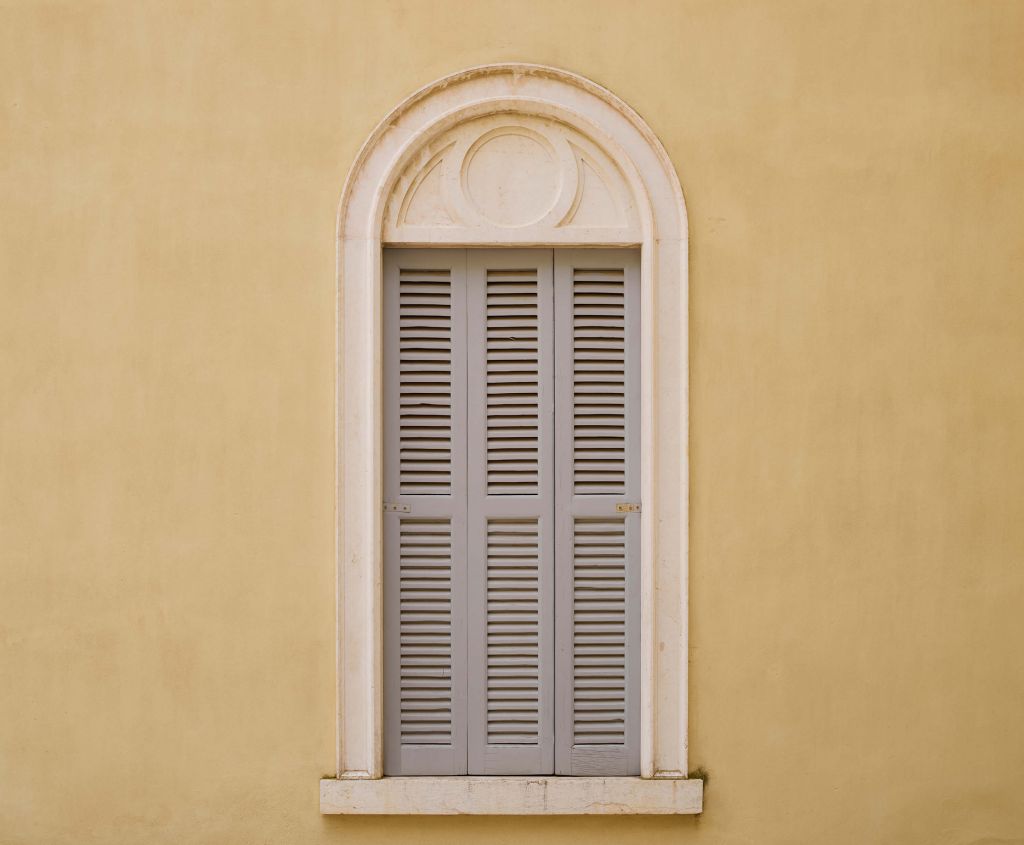 Ventana con contraventanas de madera sobre pared amarilla