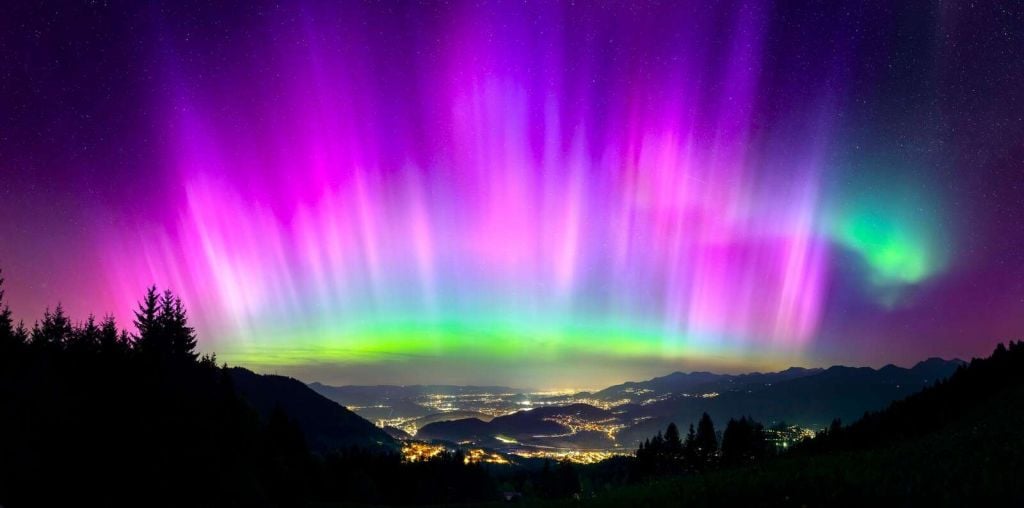 Aurora boreal sobre ciudad montañosa iluminada.
