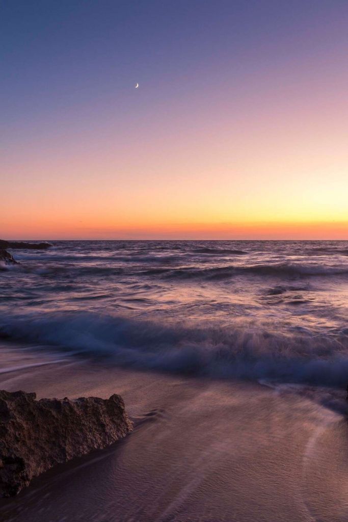 Luz de luna sobre olas moradas al atardecer.