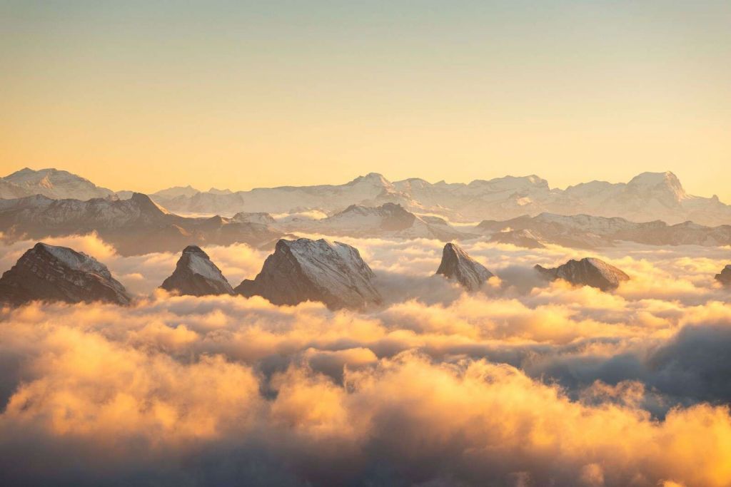 Picos de montaña sobre un mar de nubes doradas.
