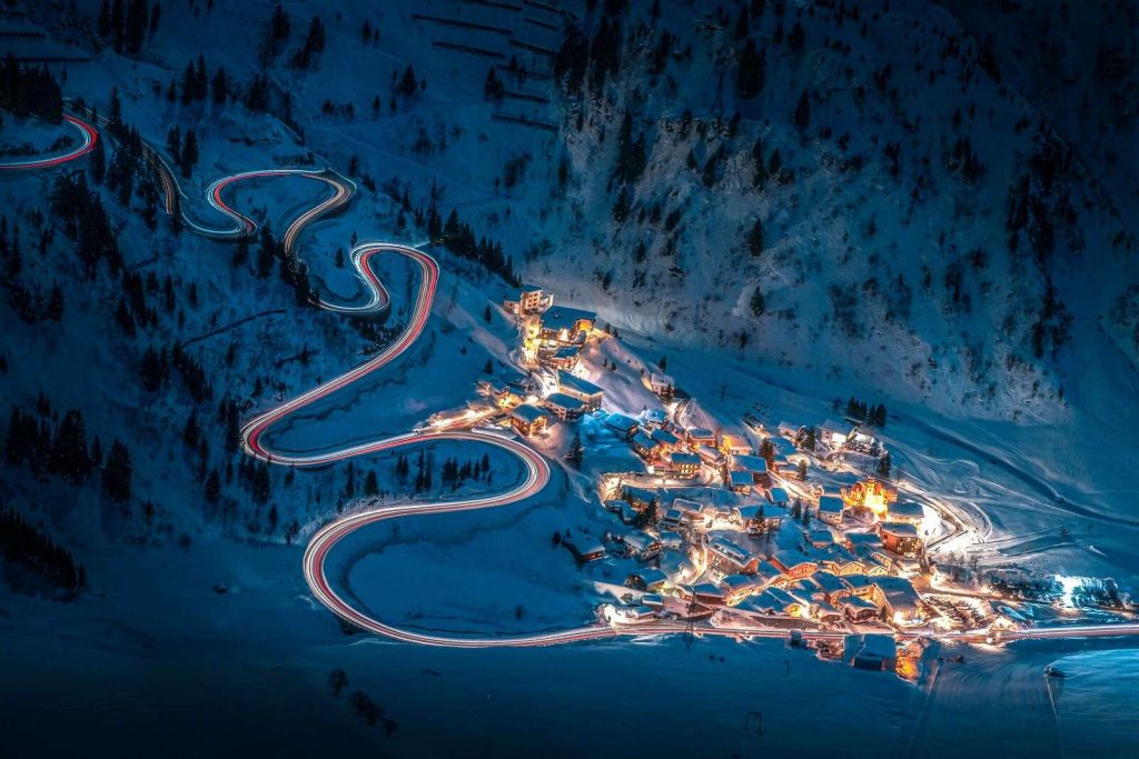 Pueblo de montaña iluminado con carretera de montaña serpenteante.