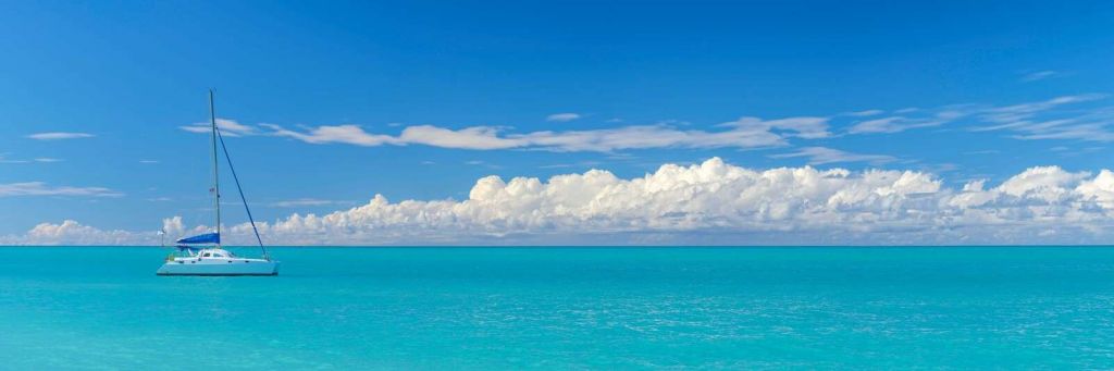 Vista panorámica de un paisaje marino azul con velero y cielo nublado.